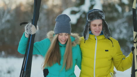 Side-view-portrait-of-active-young-couple-carrying-skis-chatting-on-the-way-back-in-beautiful-winter-forest,-copy-space